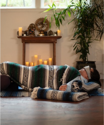 Student resting in a supported restorative pose surrounded by candlelight